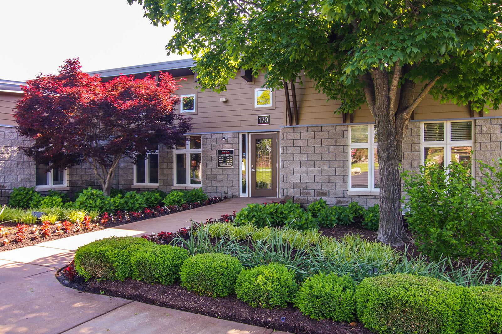 Rockwood Apartments A building entrance with neatly trimmed bushes, trees, and landscaped greenery along a concrete path.