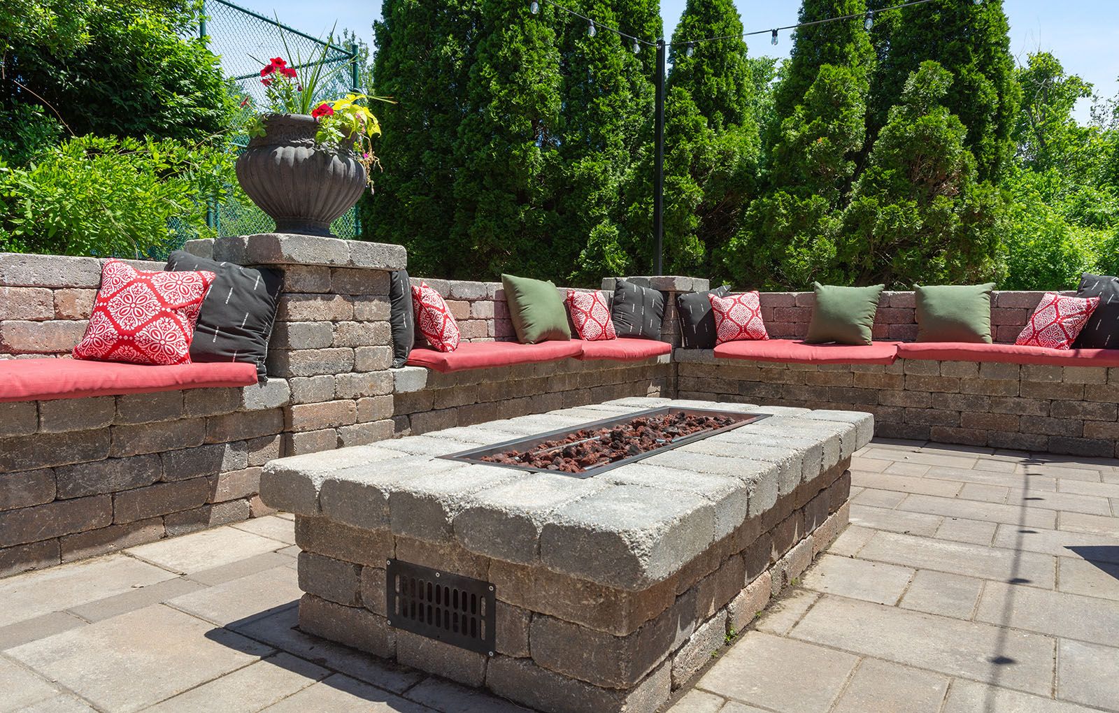 Rockwood Apartments Stone patio with built-in seating, red and green cushions, and a rectangular fire pit in the center.