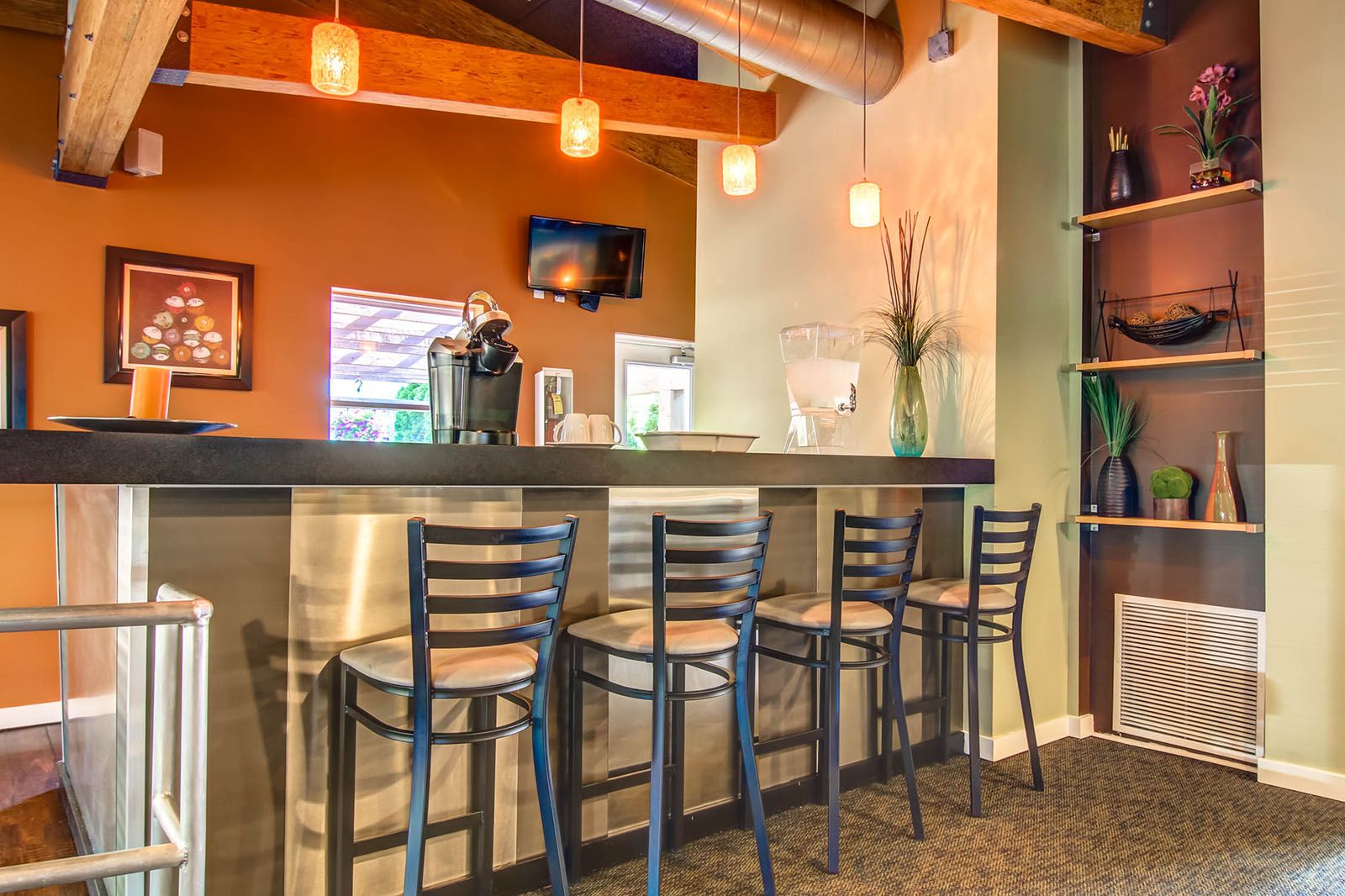 Rockwood Apartments Modern bar area with four black chairs, overhead pendant lights, and shelves with decorative items.