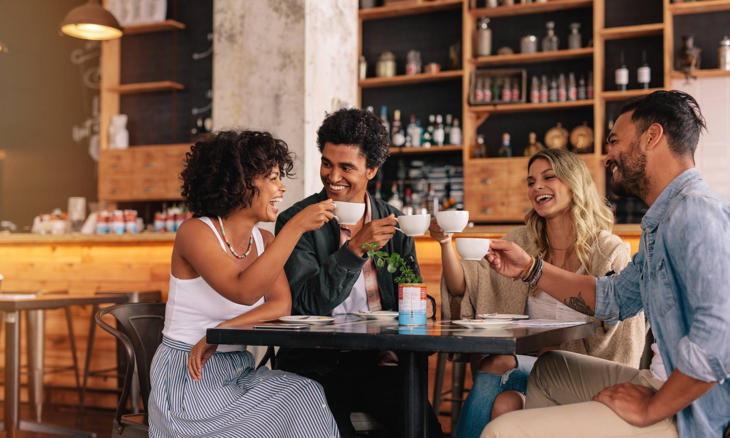 Rockwood Apartments Four friends sit at a café table, smiling and clinking coffee cups together in a cheerful toast.