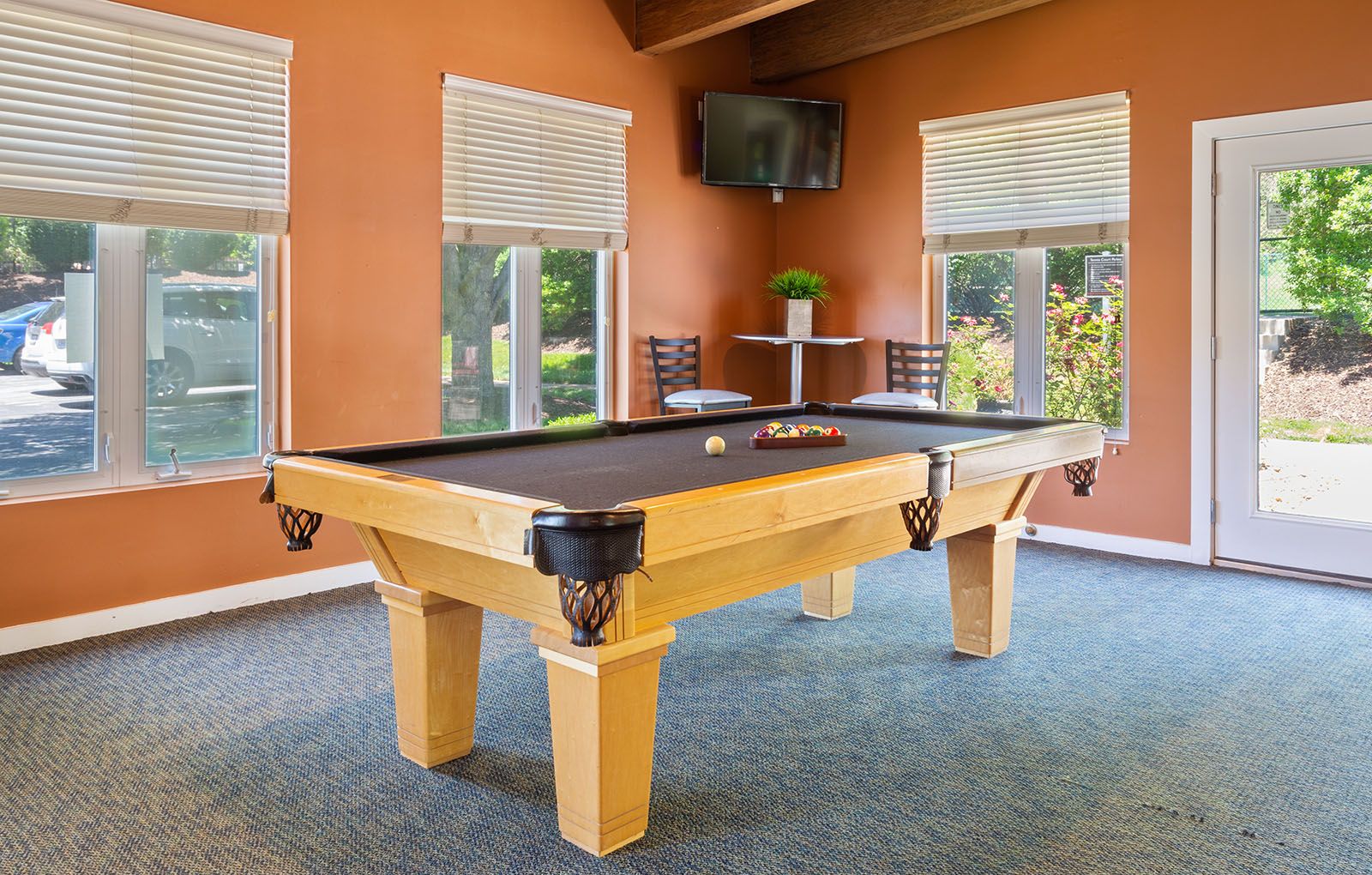 Rockwood Apartments A pool table set for a game in a sunlit recreation room with orange walls and large windows.