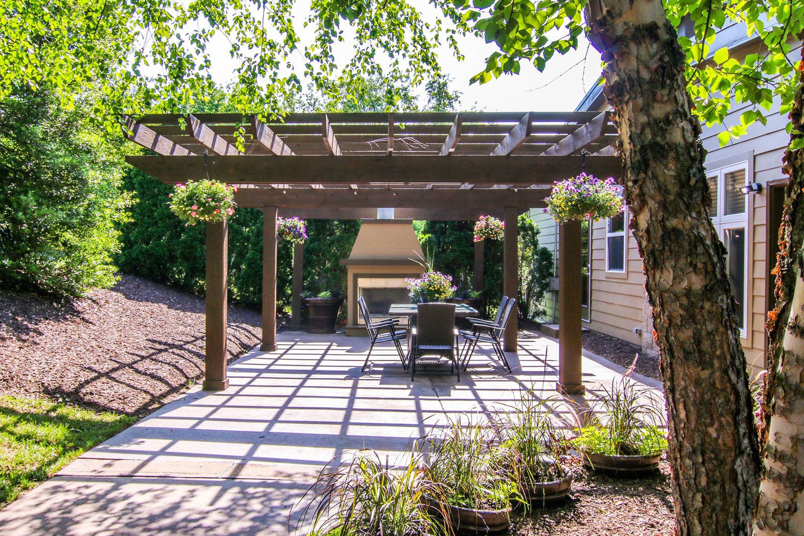 Rockwood Apartments A patio with a pergola, outdoor dining set, fireplace, hanging plants, and surrounding trees.