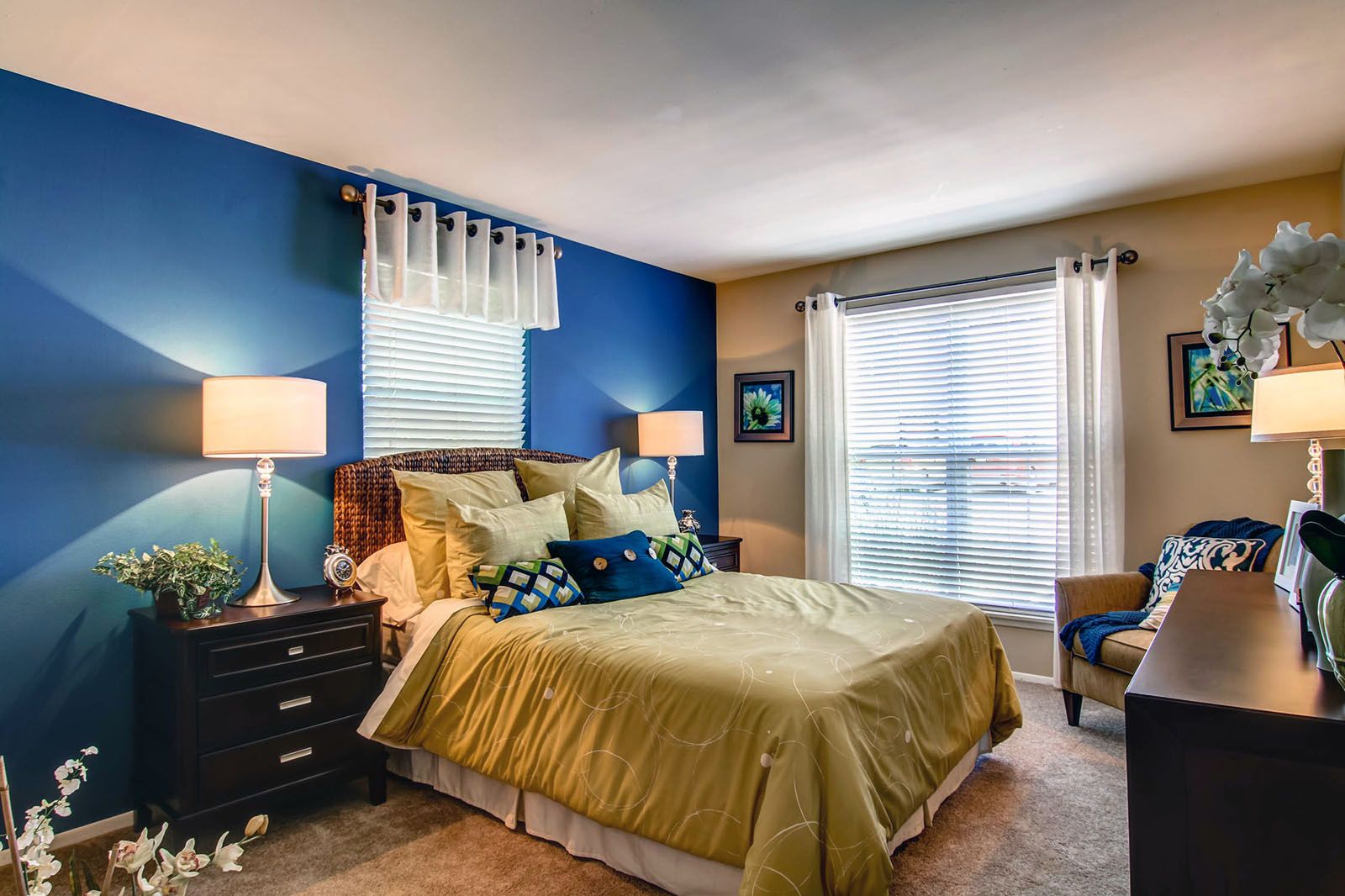 Rockwood Apartments Modern bedroom with blue accent wall, large window, double lamps, and a neatly made bed with yellow bedding.