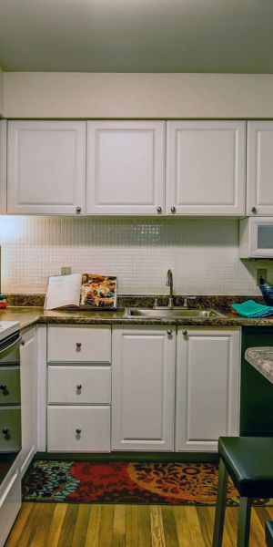 Rockwood Apartments Small kitchen with white cabinets, a fridge, stove, bar counter, and colorful decor on walls and counters.