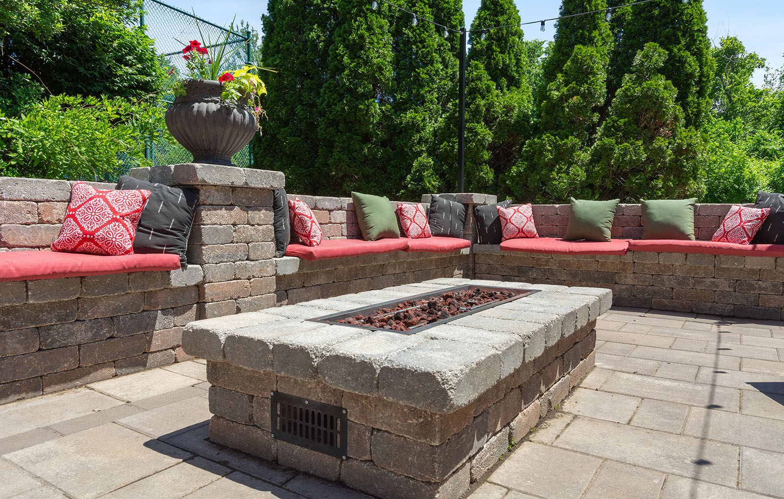 Rockwood Apartments Stone patio with built-in seating, red and green cushions, and a rectangular fire pit in the center.